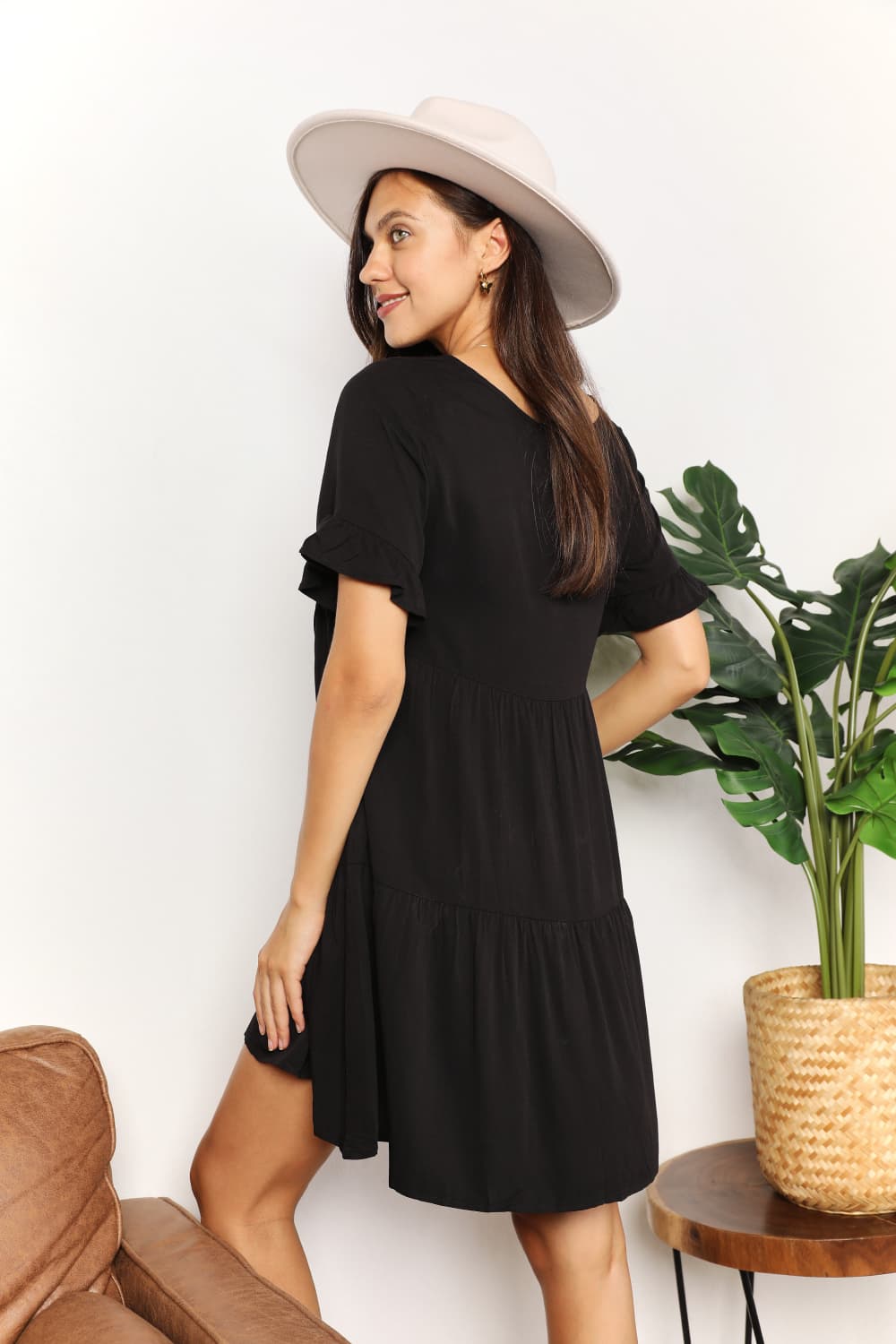 "Model wearing the black Mandy tiered V-neck mini dress, back view."