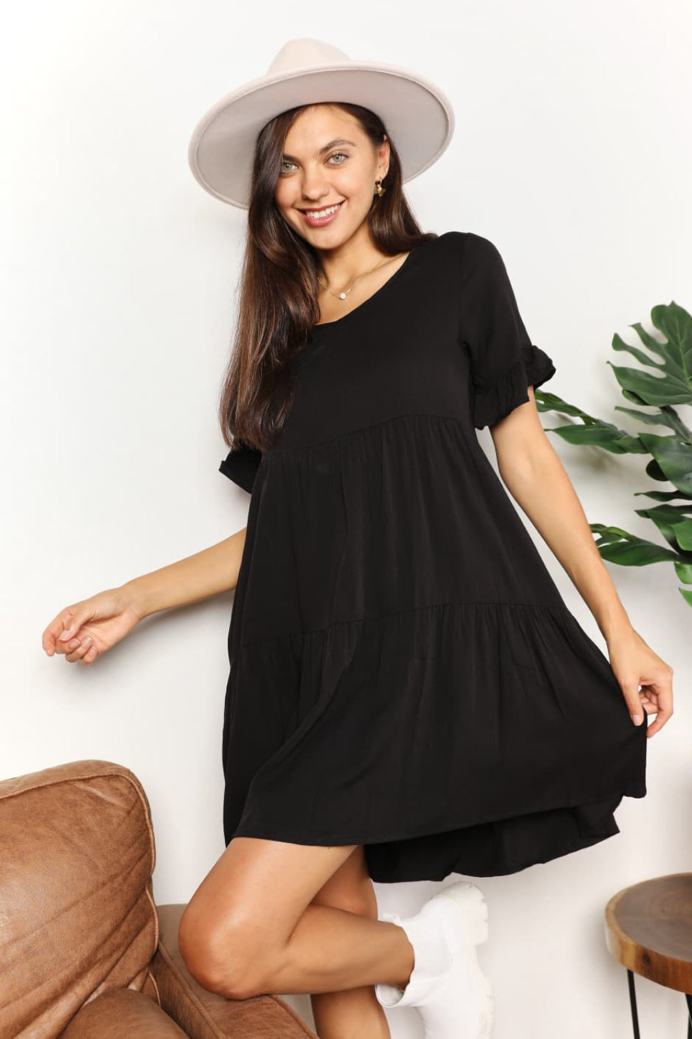 "Model wearing the black Mandy tiered V-neck mini dress with flounce sleeves, seated full-length view."