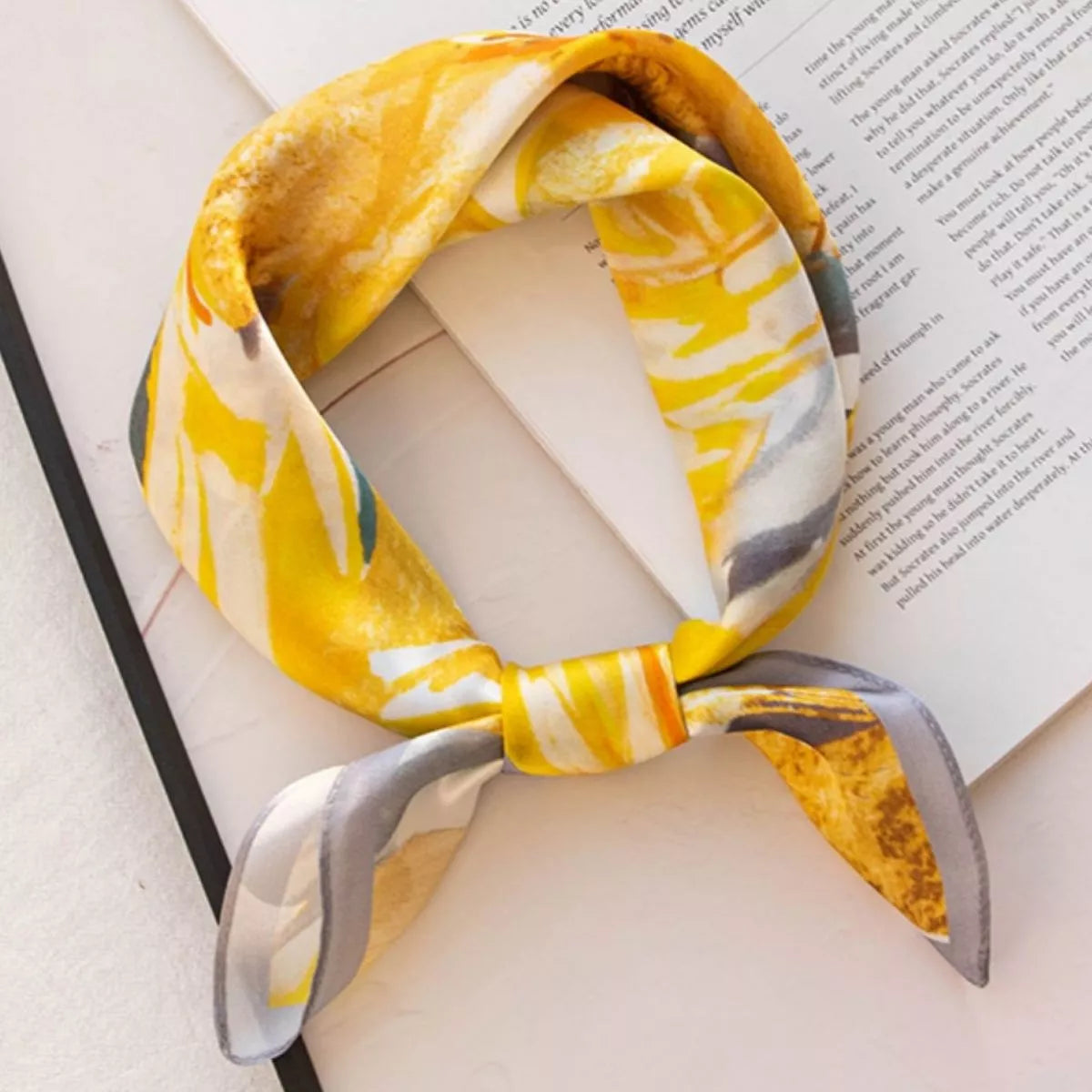 Sherbet yellow floral square scarf tied in a loop on an open book.