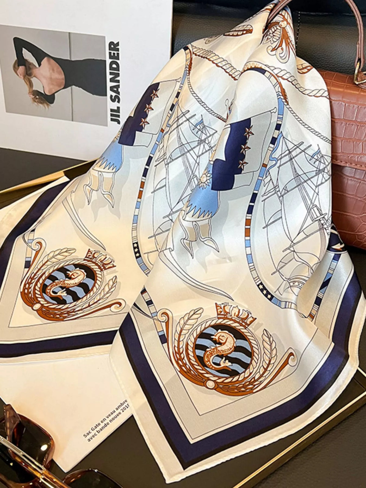 Ivory nautical scarf draped beside a brown handbag, showing rope and ship motifs.
