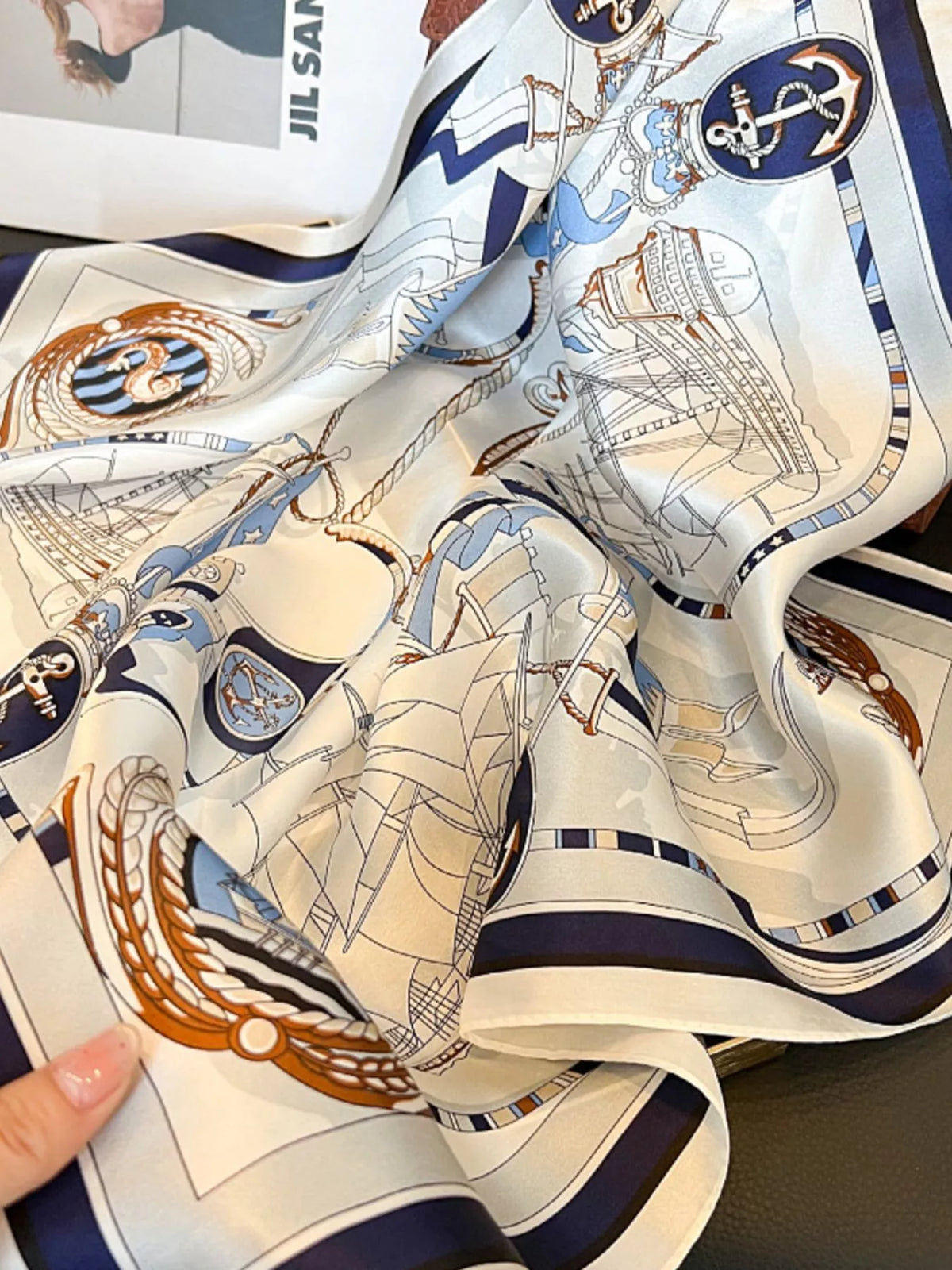 Close-up of ivory scarf folds with sailing ships, anchors, and a navy border.