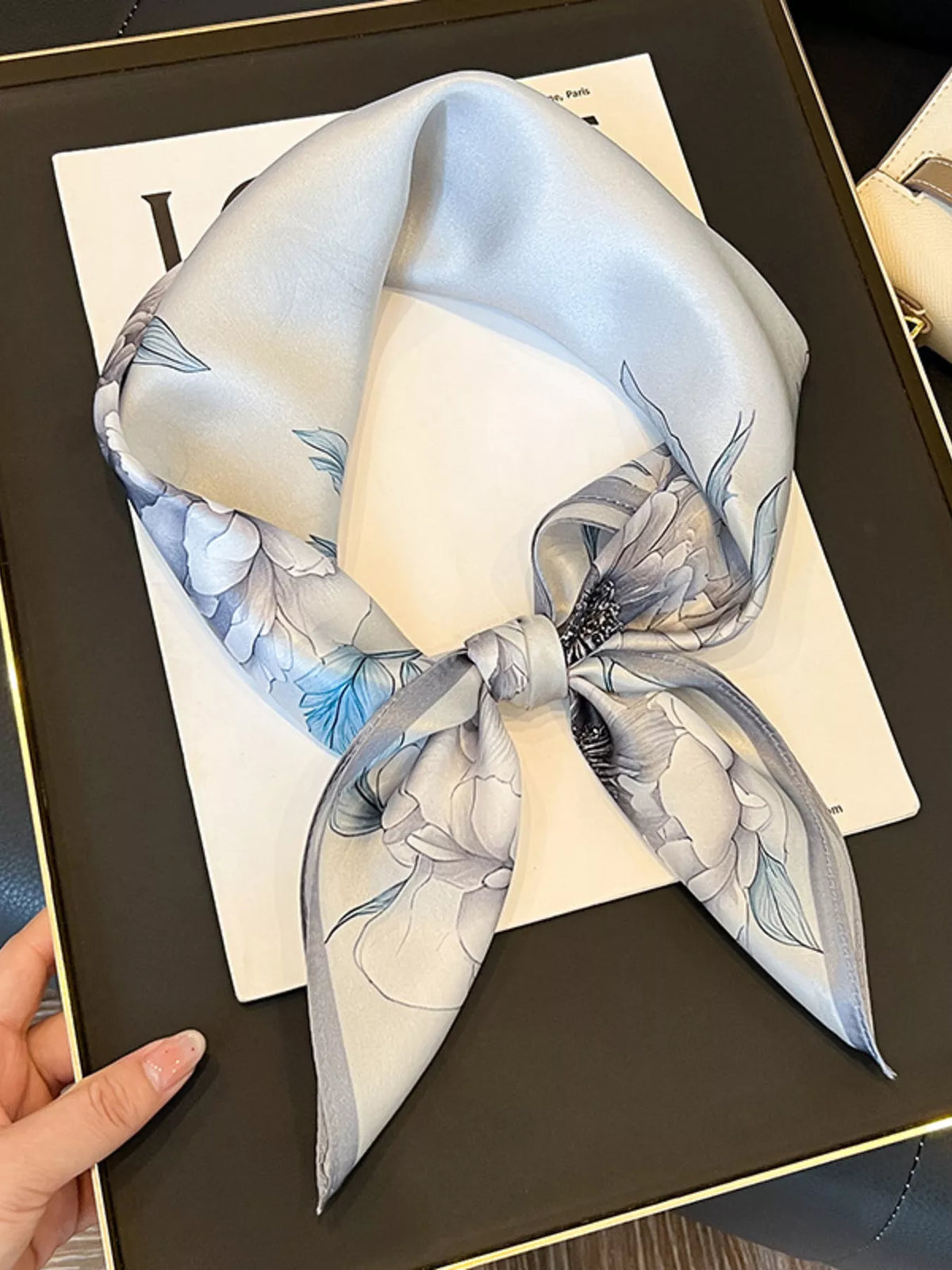 Light gray floral square scarf tied in a loop on a magazine.