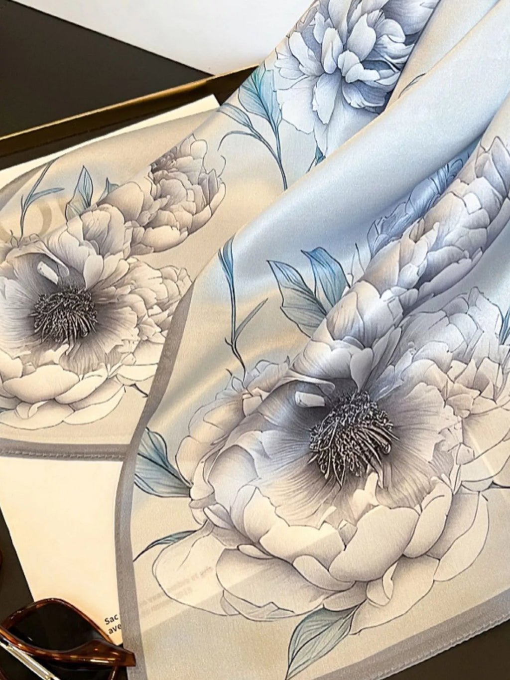 Close-up of large gray flowers and blue-toned leaves on the draped scarf.