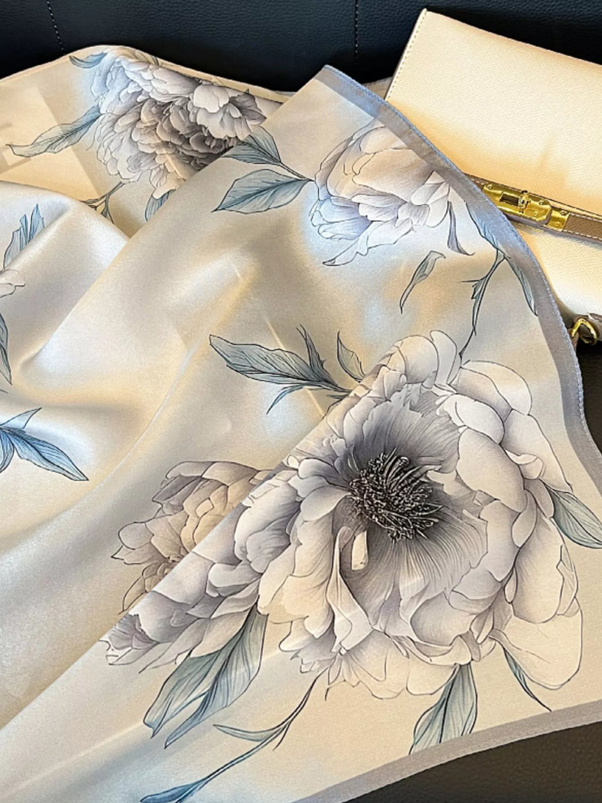 Gray floral scarf spread beside an ivory handbag, showing large blooms and a gray border.