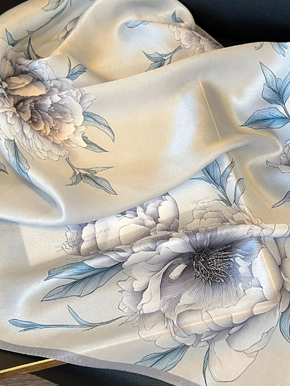 Close-up of gray floral blooms and blue-toned leaves across scarf folds.