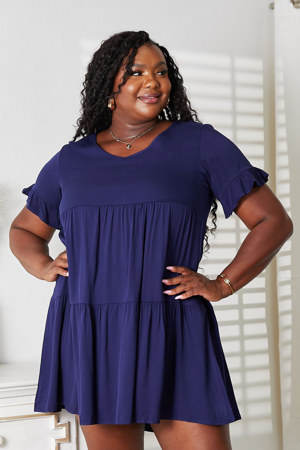 "Plus-size model wearing the dark blue Mandy tiered V-neck mini dress with flounce sleeves, front view."