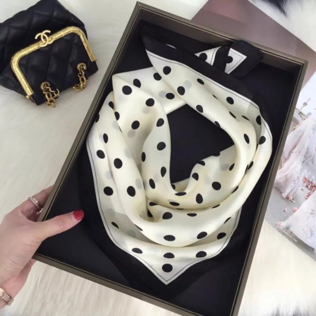 Cream white polka dot silk scarf loosely looped in a display tray