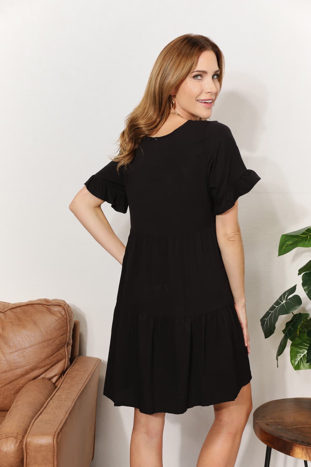  "Model wearing the black Mandy tiered V-neck mini dress, three-quarter back view showing the flounce sleeves."
