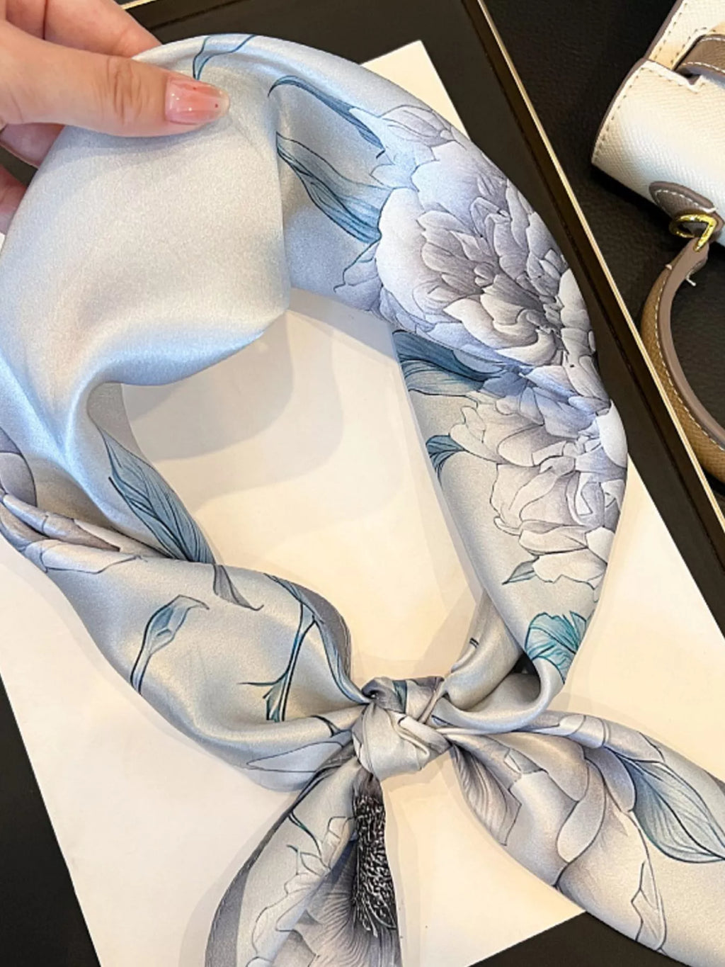 Hand holding a knotted light gray floral scarf over a magazine.