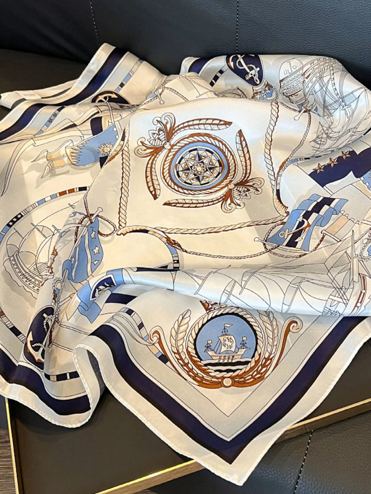 Nautical square scarf spread over a dark surface with compass, anchor, and sailing ship motifs.