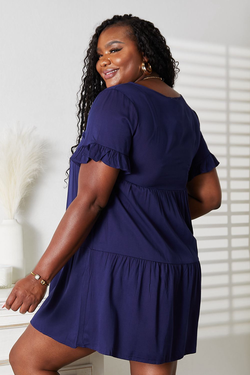 Plus-size model wearing the dark blue Mandy tiered V-neck mini dress, side view."
