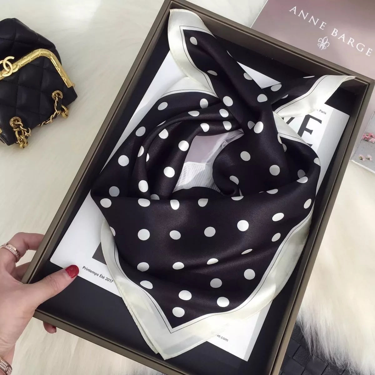 Black silk scarf with white polka dots and a contrasting cream border loosely looped in a tray