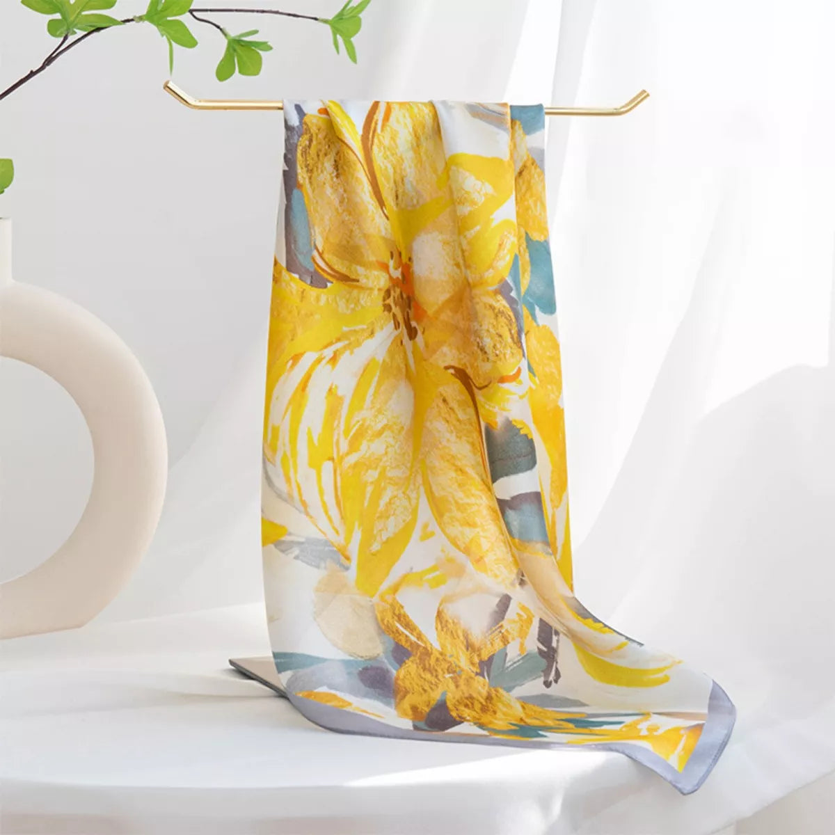 Yellow floral square scarf with gray edging draped over a gold display stand.