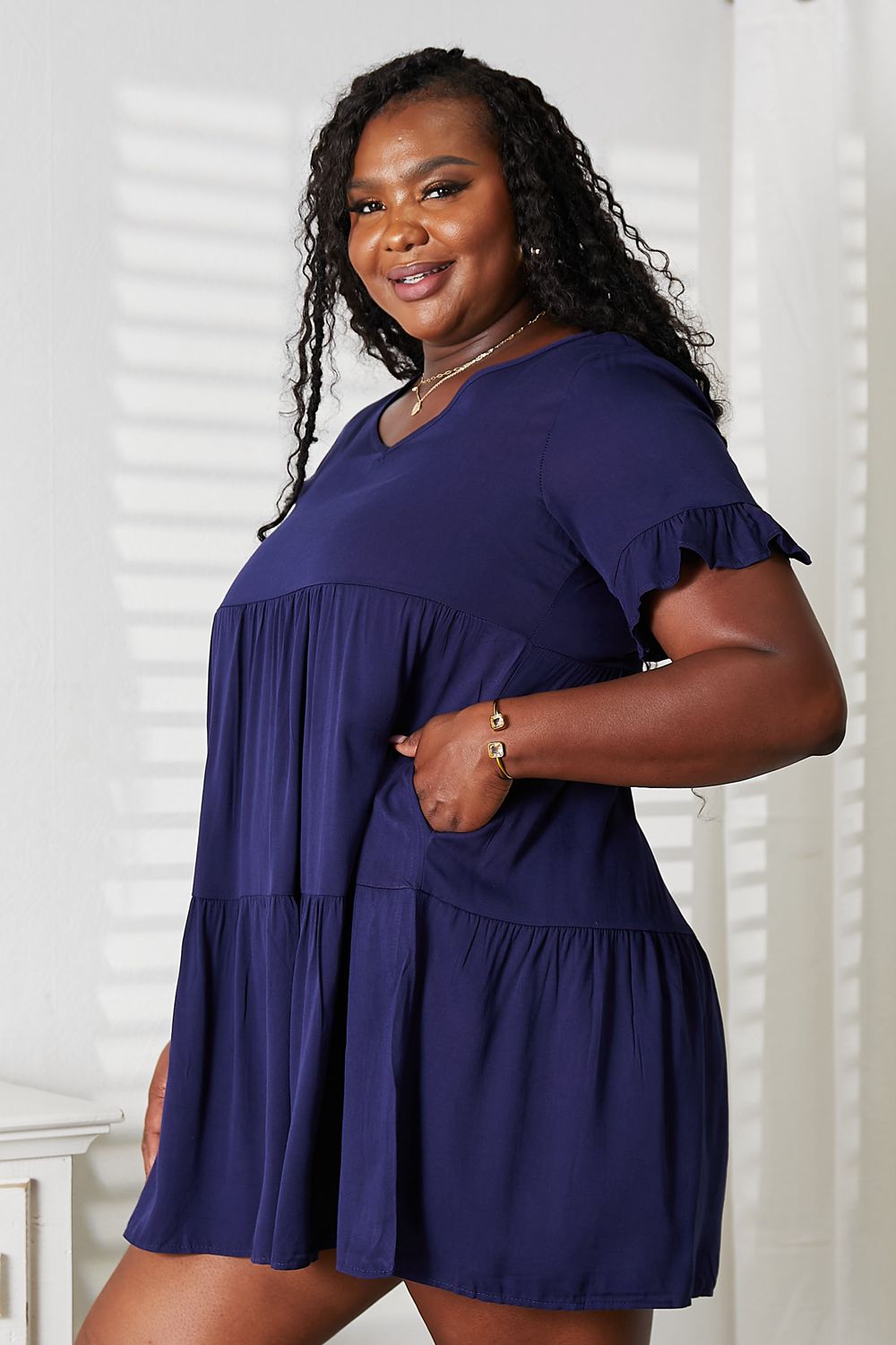Plus-size model wearing the dark blue Mandy tiered V-neck mini dress, side view