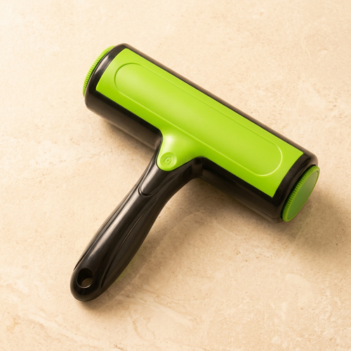 Green and black two-way pet lint roller on a cream stone surface